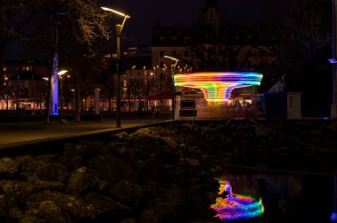 Gece lunaparkta atlı karınca. Suda yansıma. Uzun pozlama ışığı. Ouchy, Lozan, İsviçre.