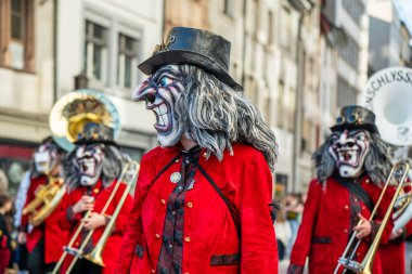 Basel, İsviçre - 25 Mart 2026: İsviçre 'nin tarihi kent merkezinde düzenlenen Basel Fasnacht geçit töreni sırasında geleneksel kırmızı kostümler giyen maskeli karnaval müzisyenleri.