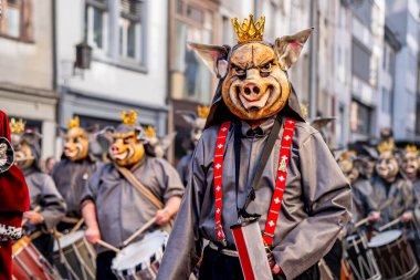 Basel, İsviçre - 25 Mart 2026: Tarihi Basel kent merkezinde düzenlenen geleneksel Basel Fasnacht geçit töreninde domuz kral maskesi takan ve altın taç takan karnaval davulcusu.