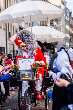 Basel, İsviçre - 25 Mart 2026: İsviçre 'nin en ünlü karnaval festivali olan Basel Fasnacht geçit töreninde geleneksel maskeli karnaval karakterleri bisiklet arabalarına biniyor ve kalabalıkla etkileşime giriyorlar.