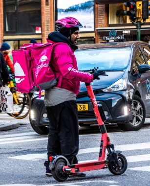 İsveç 'in merkezindeki Foodora i Stockholm şirketinden yiyecek teslimatı yapan elektrikli scooterlı bir kurye..