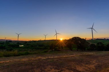 Rüzgar türbinleri günbatımında rüzgardan elektrik üretmek için park ederler.