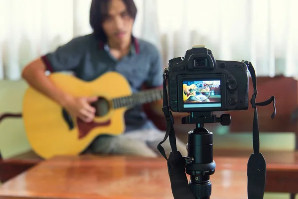 The man recording video clip of his playing guitar by camera on tripod