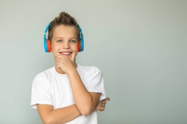 Handsome boy in a white T-shirt listens to music with headphones. A teenage boy looks into the frame, a charming smile, his eyes shine.Isolated on a gray background.