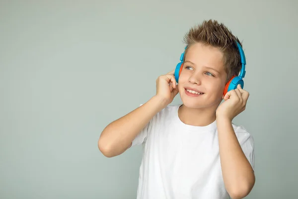 Handsome boy in a white T-shirt listens to music with headphones. The teenager enjoys the music, his eyes are quite glittering. Isolated on a gray background. Large portrait.