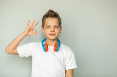 Gri gözlü bir çocuğun portresi parmaklarından tamam işareti gösteriyor. Genç kızın boynunda kulaklık var. Beyaz gömlekli adam. İzole edilmiş. Gri arkaplan.