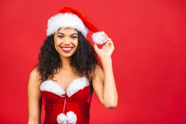 Güzel gülümseyen mutlu Afro-Amerikan siyah kadın Noel Baba kıyafetleri içinde kırmızı arka planda izole edilmiş. Yeni yıl ve Noel konsepti. 