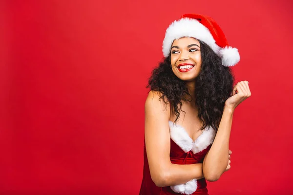 Güzel gülümseyen mutlu Afro-Amerikan siyah kadın Noel Baba kıyafetleri içinde kırmızı arka planda izole edilmiş. Yeni yıl ve Noel konsepti. 