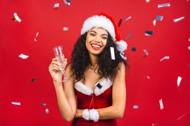Güzel gülümseyen mutlu Afro-Amerikan siyah kadın Noel Baba kıyafetleri içinde kırmızı arka planda izole edilmiş. Yeni yıl ve Noel konsepti. 