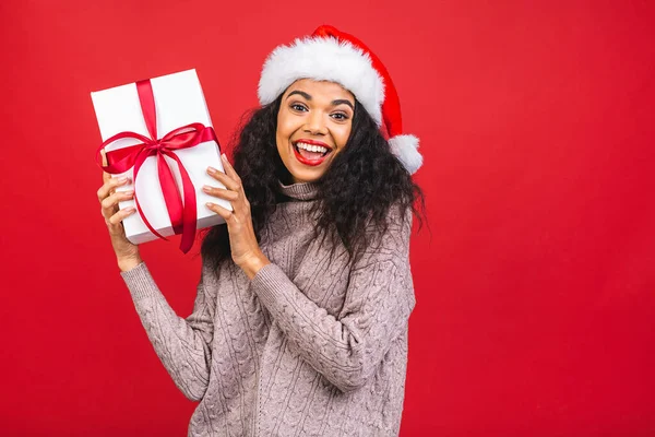サンタクロースの服で美しい笑顔幸せなアフリカ系アメリカ人の黒人女性は 赤の背景に隔離された 新年とクリスマスのコンセプト ギフトボックスの保持 — ストック写真