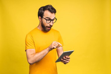 Dijital tablet kullanan mutlu sakallı adam sosyal medya haberlerine şaşırdı, şaşıran müşteri şaşırdı. Çevrimiçi galibiyetin heyecanı sarı arka planda izole edildi..