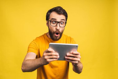 Dijital tablet kullanan mutlu sakallı adam sosyal medya haberlerine şaşırdı, şaşıran müşteri şaşırdı. Çevrimiçi galibiyetin heyecanı sarı arka planda izole edildi..