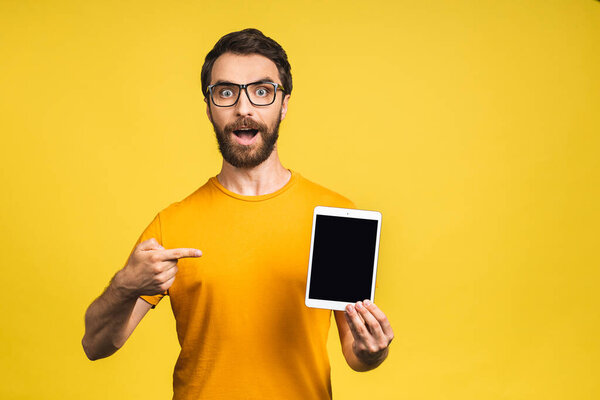 Product presentation. Promotion. Young bearded man holding in hands tablet computer with blank screen. Isolated over yellow background.