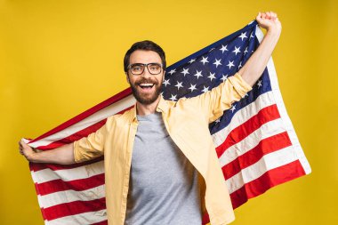 Sarı arka planda izole edilmiş Amerikan bayrağı taşıyan sakallı mutlu bir adamın portresi..