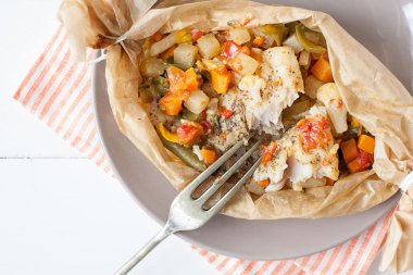 fried fish with vegetables in parchment clipart