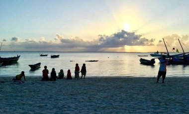 Zanzibar 'da gün batımında sahilde okyanus, tekne ve insan siluetleri olan bir manzara. 
