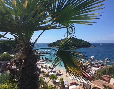 Arnavutluk 'un Ksamil kentinde palmiye ağacı ve plajlı yaz manzarası 