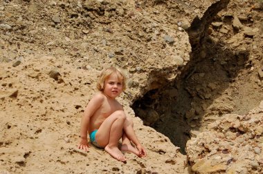 Yaz tatilinde kayalık sahilde oturan çocuk. 