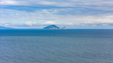 Sonsuz mavi denizin ortasında belirgin bir bulut formasyonuyla taçlandırılmış ıssız bir volkanik ada..