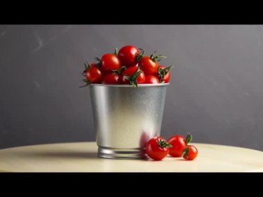 Tahta bir masanın üstünde, bir kova taze kırmızı kiraz domatesinin etrafında dönüyor. Yan görüş. Hasat et. Doğal yiyecek..