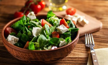 Ahşap bir tahtanın üzerinde (Valerianella Locusta) seramik bir kasede marul yapraklı mung fasülyesi, peynir ve kiraz domatesinden salata. Diyet ve sağlıklı beslenme, vejetaryenlik. Yumuşak odaklanma. keto diyeti 