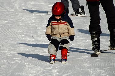 Üç yaşındaki küçük bir çocuk kayak merkezinde kayak yapmayı öğreniyor..