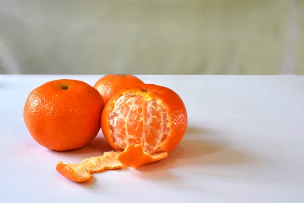 Três Mandarinas Uma Das Quais Meio Descascada Uma Mesa Branca — Fotografia de Stock