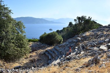 Genç bir kadın antik bir amfitiyatronun merdivenlerinde otururken manzaraya hayran. Türkiye, Amos.