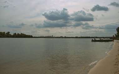 Manzara: Ufukta Kiev şehrinde demirlemiş bir teknesi olan kumlu nehir kıyısı.