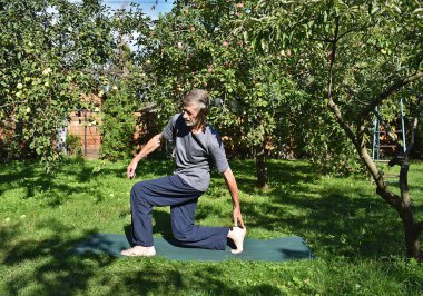 76 yaşında bir adam formda kalmak için bahçede bacak güçlendirme egzersizi yapıyor..