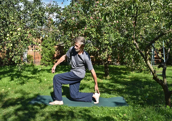 76 yaşında bir adam formda kalmak için bahçede bacak güçlendirme egzersizi yapıyor..