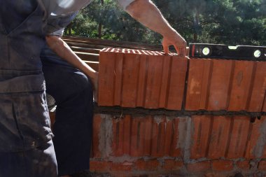 Bir adam kırmızı seramik bloklardan bir duvar inşa ediyor..