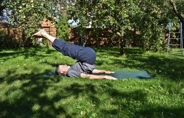 76 yaşındaki bir adam bahçesindeki karın ve sırt kaslarını güçlendirmek için egzersiz yapıyor..