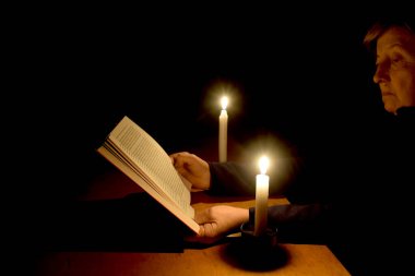 Yaşlı bir kadın mum ışığında bir kitap okur. Karartma kavramı, Ukrayna 'nın bombalanması nedeniyle kritik altyapının tahrip olmasıyla ilgilidir..