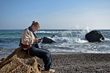 Genç bir kadın sonbaharın sonlarında fırtınalı bir denizin kıyısında dinleniyor..