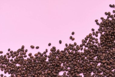 Arka plan olarak pembe renkli yüzeyde kavrulmuş ve aromatik kahve çekirdekleri. Üst görünüm ve metin için boşluk kopyala. Taze Arabika kahvesinin makro fotoğrafı....