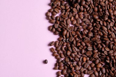 Arka plan olarak pembe renkli yüzeyde kavrulmuş ve aromatik kahve çekirdekleri. Üst görünüm ve metin için boşluk kopyala. Taze Arabika kahvesinin makro fotoğrafı....