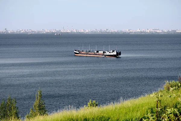 Freight ship sailing on a river in sunny summer day. Cityscape on background. Concept of Navigation and commerce shipping.