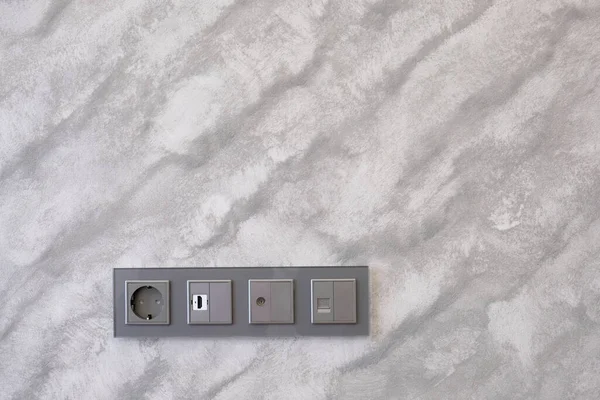 Modern and technological sockets on grey textured wall. Decorative plaster. Concept of electricity, apartment renovation and interior design.