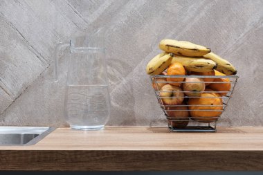 Masanın üstünde su ve metal meyve sepeti olan cam sürahi. Mutfaktaki Durgun Hayat kavramı.