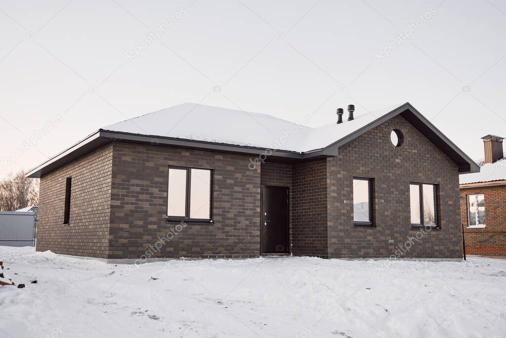 One-story brick house on the background of a snowy winter evening. Construction of low-rise buildings for further sale. Concept of building business.