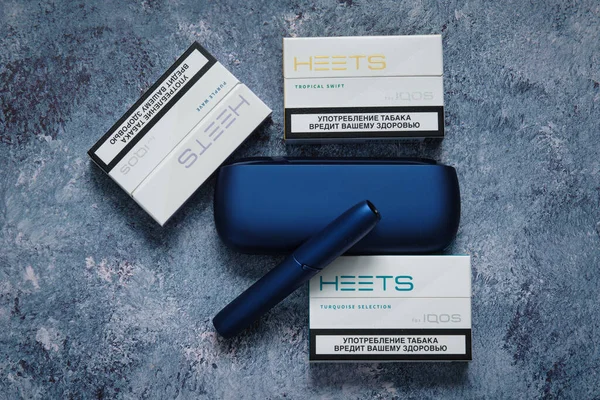 Kazan, Tataristan, Rusya - Aralık 2020: Arka plan olarak grunge mavi yüzey üzerinde turkuaz, mor ve tropikal süratli IQOS elektronik sigarası. Resmi kapat..