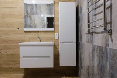 Modern tuvalet içi gri, bej ve beyaz renklerle tasarlandı. Lavabo, ayna, havlu kurutma makinesi ve dolap. Su deposu. Gayrimenkul kavramı.