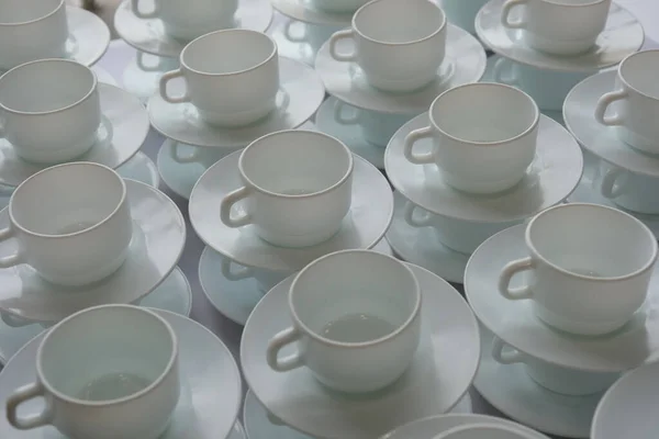 Pattern of a group of empty white cups and  sausers for coffee and tea, standing in line of each other on table  to serve for breakfast or buffet at catering. Selective focus
