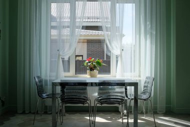 Masa ve sandalyeler mutfaktaki büyük pencereye karşı. Çiçekli vazo. Modern iç mekan kavramı 