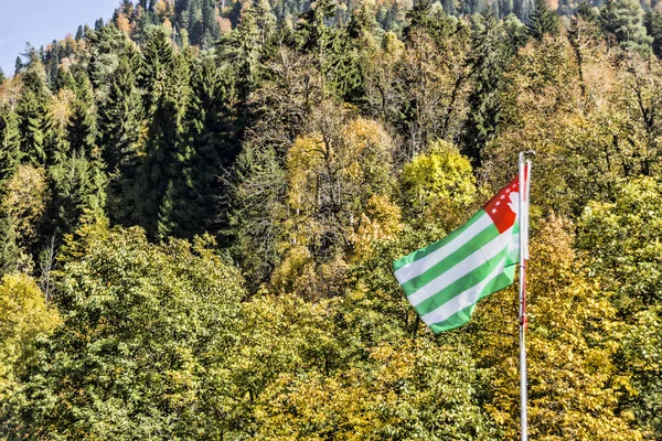 The flag of Abkhazia develops over the autumn mountains. — Stock Photo, Image