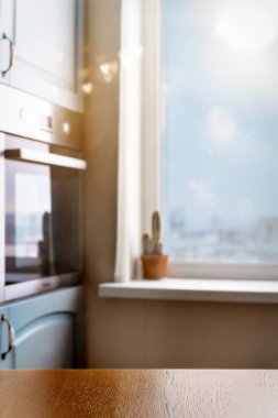 Ahşap masa yüzeyi, yumuşak sabah ışığı ve bulanık pencere arkaplanı olan parlak minimalist mutfak. Metin veya tasarım için kopya alanı olan rahat ev sahnesi.