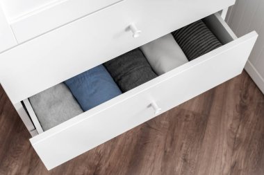 Beyaz çekmecede düzgünce katlanmış kıyafetlerin üst görüntüsü. Modern ev organizasyonu ve kostüm depolama konsepti.