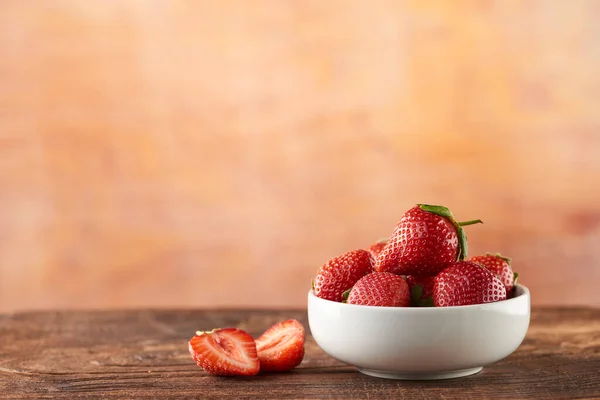 Strawberries with strawberry leaf on a White bowl and wooden table with defocused nature background by the window.