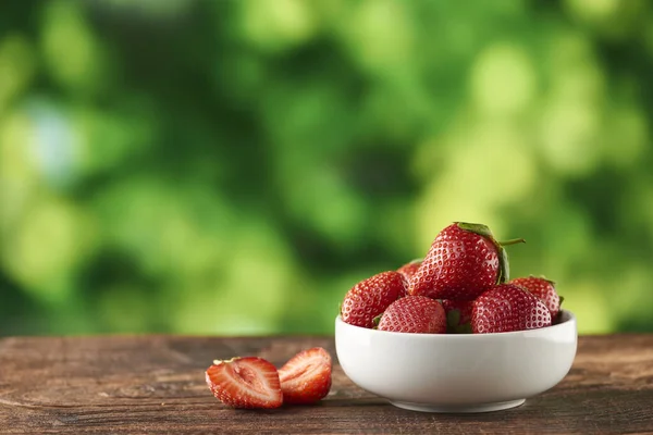 Strawberries with strawberry leaf on a White bowl and wooden table with defocused nature background by the window.